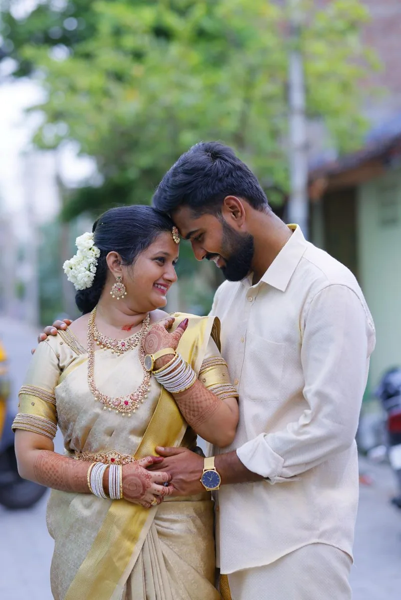 Rajavel and Nivethidha in cream and gold wedding clothes, foreheads together, both laughing